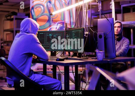 Hackers planning malware attack on government computer network system and coding ransomware. Criminals programming malicious software to hack database server in abandoned warehouse Stock Photo