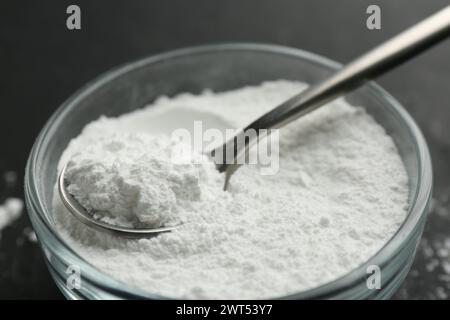 Baking powder in bowl and spoon on black table, closeup Stock Photo