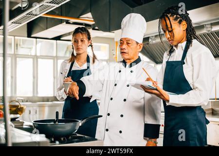 Professional Asian senior chef teaches diverse students cooking in a restaurant kitchen. Emphasis on Stock Photo