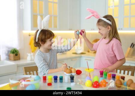 Easter celebration. Cute children with bunny ears having fun while painting eggs at white marble table in kitchen Stock Photo