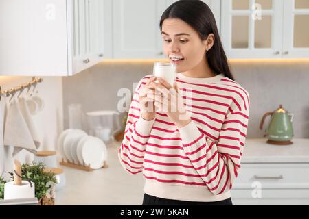 Cute woman with milk mustache drinking tasty dairy drink in kitchen. Space for text Stock Photo