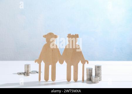 Pension savings. Figure of senior couple and coins on white wooden table Stock Photo