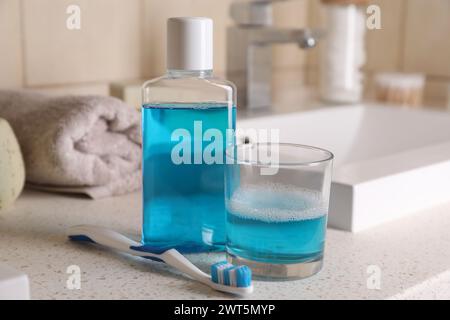 Fresh mouthwash in bottle, glass and dental floss on countertop in bathroom, closeup Stock Photo