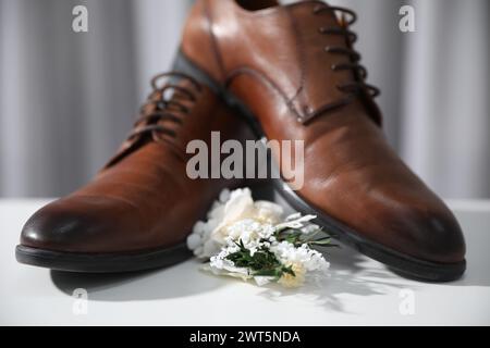 Wedding stuff. Stylish boutonniere and brown shoes on white surface against gray background, closeup Stock Photo