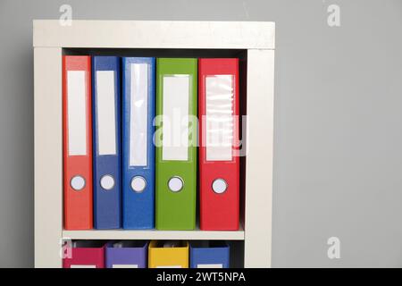 Colorful binder office folders on shelving unit near light grey wall. Space for text Stock Photo