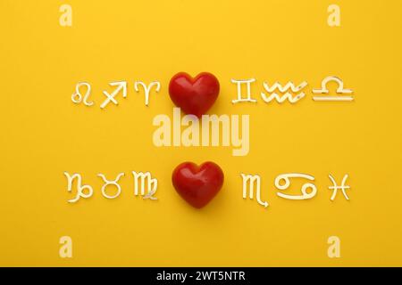 Zodiac compatibility. Signs with red hearts on yellow background, flat lay Stock Photo