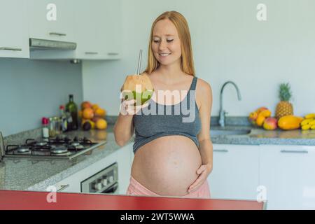 Quenching her pregnancy thirst with a refreshing choice, a pregnant woman joyfully drinks coconut water from a coconut in the kitchen, embracing Stock Photo