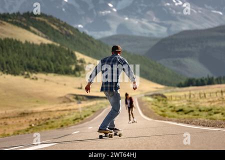 Two young skaters rides on longboards at straight mountain road Stock Photo