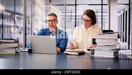 Two Businesspeople Calculating Invoice In Office While Using Laptop Stock Photo