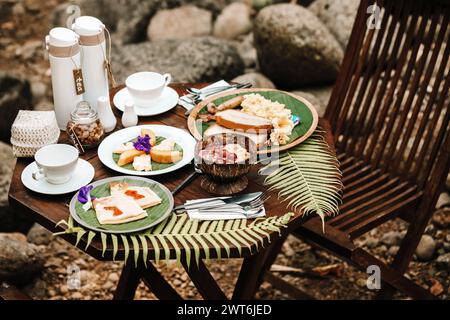 a breakfast consisting of tropicl fruits, acai bowl, crepes and toast with tea and coffee, set in a river bank Stock Photo
