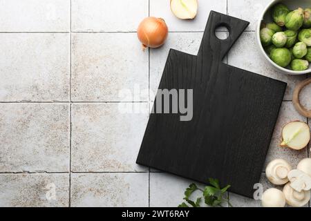 Flat lay composition with black cutting board and products on light tiled table. Space for text Stock Photo