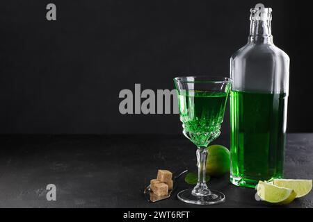 Absinthe, spoon, brown sugar and lime on black table, space for text. Alcoholic drink Stock Photo