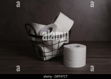 Soft toilet paper rolls in metal basket on wooden table Stock Photo