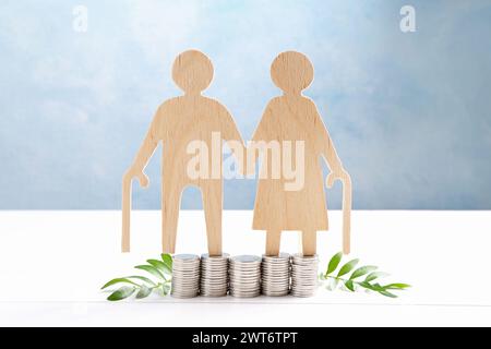 Pension savings. Figure of senior couple, stacked coins and green twigs on white wooden table Stock Photo
