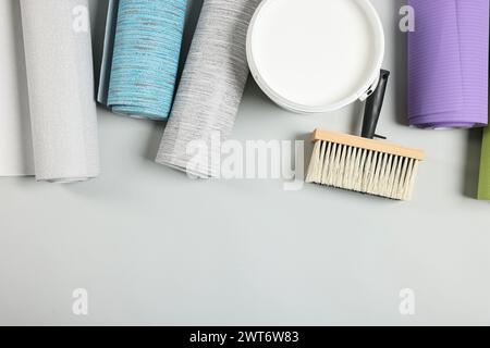 Different wallpaper rolls, brush and bucket with glue on light grey background, flat lay. Space for text Stock Photo