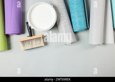 Different wallpaper rolls, brush and bucket with glue on light grey background, flat lay. Space for text Stock Photo