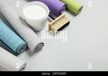 Different wallpaper rolls, brush and bucket with glue on light grey background, above view. Space for text Stock Photo