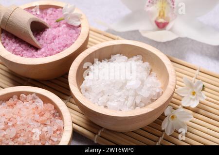 Different types of sea salt and flowers on light table, closeup. Spa products Stock Photo