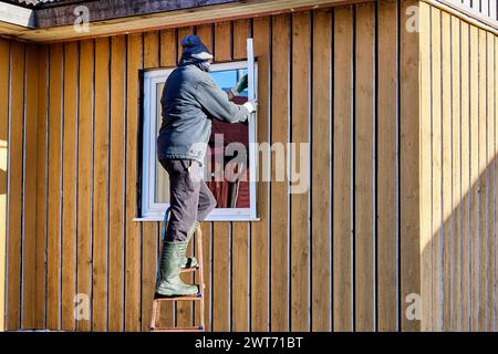 Installation exterior metal slopes on window, roofing contractor standing on step ladder on fall day. Stock Photo