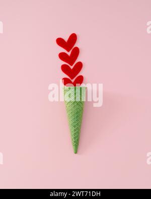 Summer love cream. Creative layout made with red hearts and green waffle ice cream cone on pink background. Minimal summertime love concept. Stock Photo