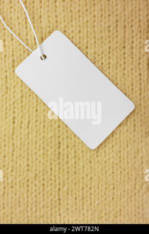 Blank clothing label on yellow knitted sweater background. Mockup, template with empty rectangular card, cloth tag for price or text. Shopping, sale, Stock Photo