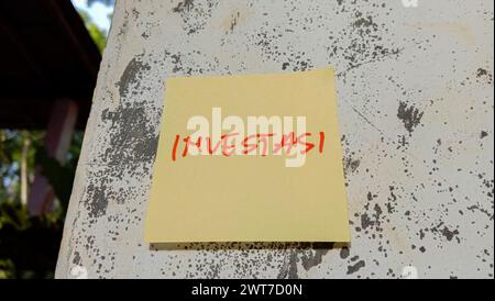 Text with the words "investasi" on a note pasted on the wall Stock Photo