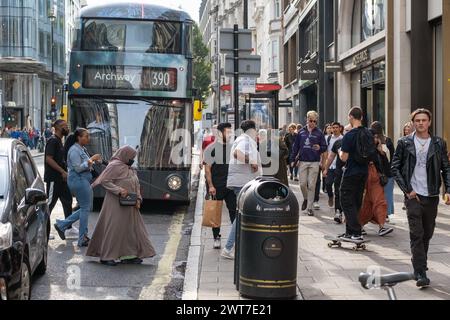 The 390 bus at a bus stop on Oxford Street, London. The scene is busy with pedestrians crossing the road and walking past the shops. Stock Photo