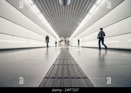 Subway station walkway tunnel - low angle view. Perspective view of silver tube corridor between underground platforms. Tactile directional blocks. Stock Photo