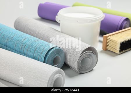 Different wallpaper rolls, brush and bucket with glue on light background Stock Photo