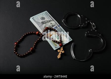 Dollars, handcuffs and prayer beads on black table Stock Photo