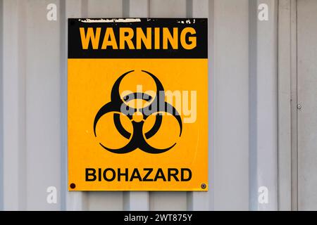 Warning sign drawn on a black and yellow placard with written in "Warning - Biohazard" with ib its middle a Biohazard symbol. Stock Photo