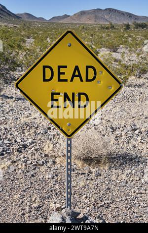 yellow and black dead end road sign in the desert with bullet holes Stock Photo