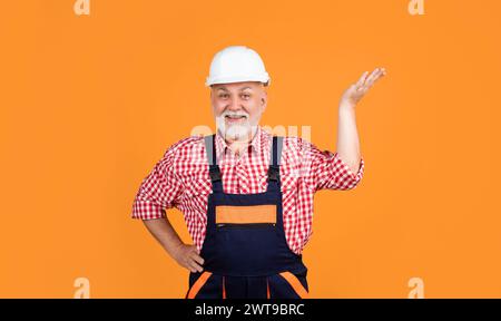 happy senior man builder in helmet on yellow background. Stock Photo