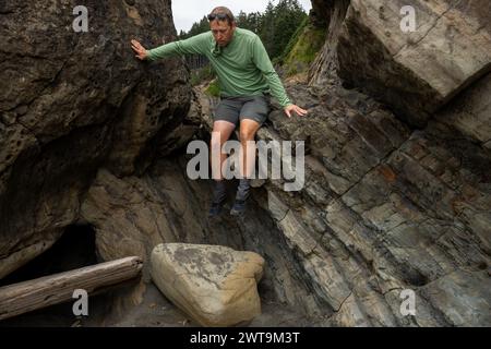 Hiker Climbs Down Rocky Formations Along Beach In Olympic National Park Stock Photo