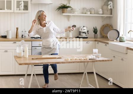 Happy mature woman in apron dancing in the kitchen Stock Photo