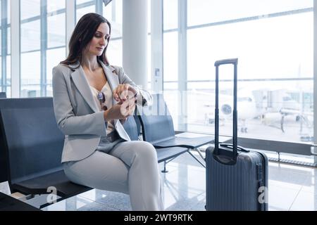 businesswoman sitting at gate of airport checking the time on her wristwatch as the flight is delayed Stock Photo