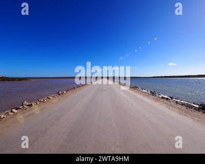 Lake MacDonnell in Eyre Peninsula, showcasing the contrast between its pink and blue waters, divided by a serene dirt road under a clear blue skies Stock Photo