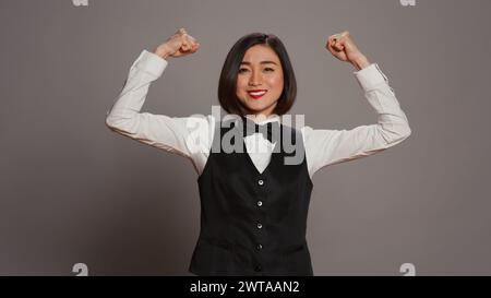 Asian hotel concierge flexing arms muscles in grey studio, showing off ...