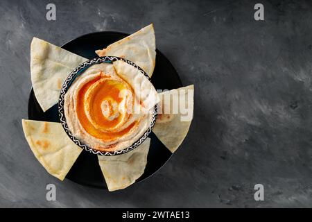 Chickpea Hummus with Pita Chips and Paprika on Dark Concrete Background, Top View, Copy Space Stock Photo