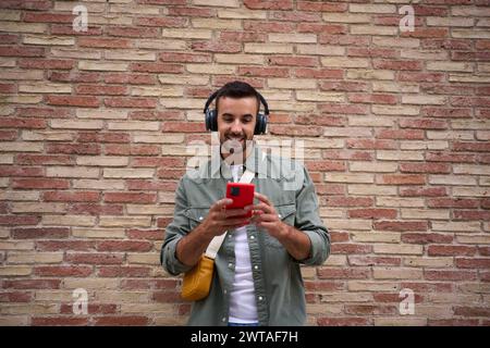 Copy space of handsome millennial man using mobile leaning against brick wall. Addicted technology.  Stock Photo