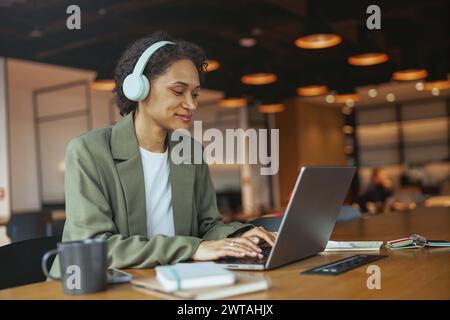 Woman iusing personal computer with headphones at table in nice modern coworking office Stock Photo