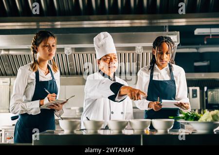 Professional Asian senior chef guides diverse students in a restaurant kitchen. Focusing on teamwork Stock Photo