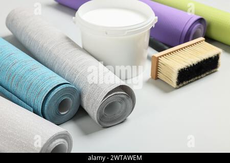 Different wallpaper rolls, brush and bucket with glue on light background Stock Photo