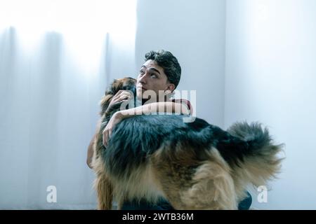A heartfelt embrace between a young Latino man and his loyal German Shepherd indoors Stock Photo