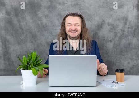 Man with long hair concentrating while utilizing a laptop in a sleek and modern office setting Stock Photo