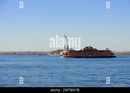 An orange ferry sails on the water near the Statue of Liberty under a clear blue sky, Manhattan, Down Town, New York City, New York, USA, North Stock Photo