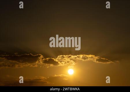 Sun shining through clouds over beach and water Stock Photo