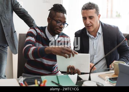 Two coworkers intently discuss work on a tablet, illustrating effective teamwork in a modern office setting. Stock Photo