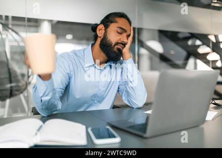 Sleepy indian guy office worker sitting at desk at office Stock Photo