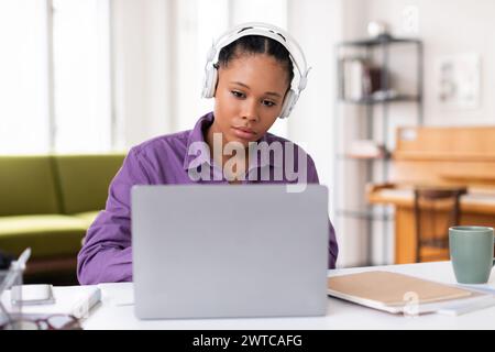 Focused black female student with headphones using laptop Stock Photo
